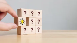 Hand placing the final puzzle block with a lightbulb icon among question-mark blocks, representing clarity and solutions
