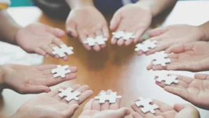 Multiple hands connecting a single puzzle piece, symbolizing teamwork and supportive real estate guidance