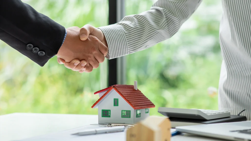 Handshake over a miniature home symbolizing Woodstock GA real estate market update and housing agreements